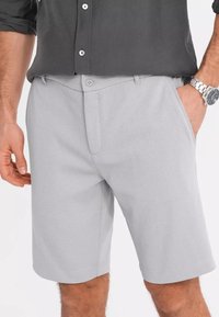 Shorts gris clair en tissu texturé, dotés d'une fermeture à bouton unique et de poches latérales. Les bords ourlés offrent une finition soignée.