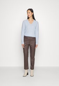 Lys blå v-hals sweater med løs pasform, parret med brune bukser. Hvide ankelstøvler med en lille hæl. Ensfarvet baggrund.