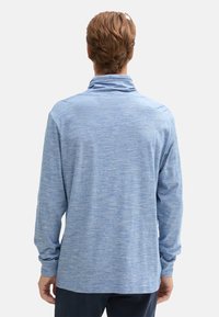 Camicia a maniche lunghe di colore blu chiaro con colletto alto, realizzata in un tessuto morbido e testurizzato. Presenta una vestibilità rilassata e un orlo arrotondato.