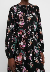 Černé květinové šaty s kulatým výstřihem, dlouhými rukávy, elastickým pasem a barevnými vzory květin a abstraktních tvarů.