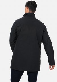 Sort lang frakke lavet af tekstureret stof med høj krave og lige snit. Frakken ender lige over knæene med diskrete syningsdetaljer.