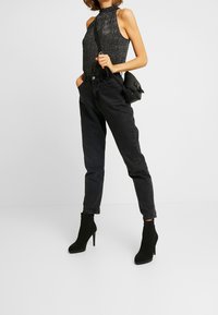 Haut dos nu noir avec une finition texturée et brillante, associé à un jean noir taille haute et des bottines à talons aiguilles noires.