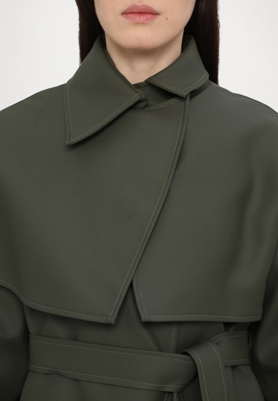 Ελιάς πράσινο παλτό με μεγάλο γιακά, ζώνη στη μέση και λεία υφή. Διαθέτει αντίθετη ραφή κατά μήκος του γιακά και των άκρων.