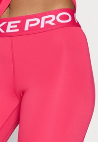 Rosa treningsbukser med bred linning som har "NIKE PRO" i hvitt. Glatt, elastisk stoff med flate sømmer for komfort.