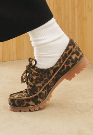 Scarpa in pelle scamosciata con stampa leopardata e lacci, dotata di una suola spessa e texturizzata. La scarpa presenta un motivo marrone e nero con punta arrotondata e dettagli marroni.
