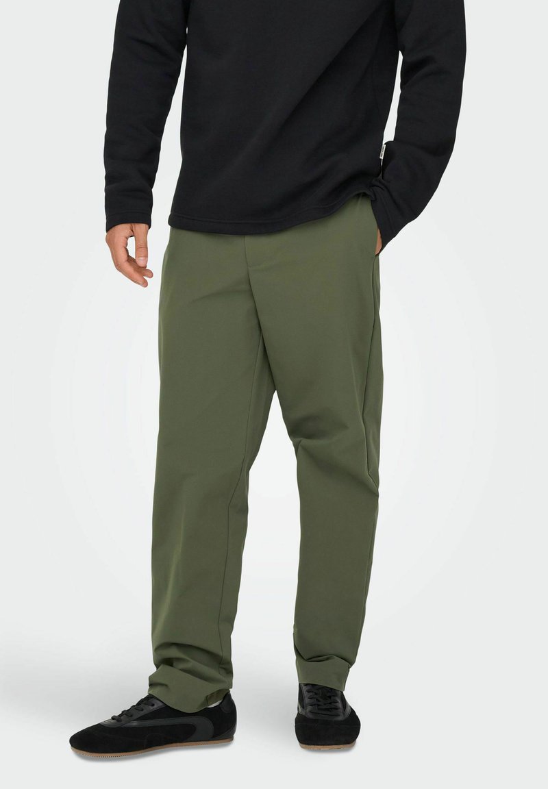 Olivgrüne Hose mit entspannter Passform, aus leichtem Material, mit seitlichen Taschen und geradem Bein, kombiniert mit schwarzen Schuhen.