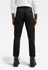 Czarne spodnie o wąskim kroju, z dwoma tylnymi kieszeniami i szlufkami na pasek, w połączeniu z czarnymi botkami za kostkę. Gładka faktura tkaniny.