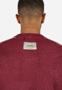 Burgundy knit sweater with a textured finish. Features a label on the back with the brand "PEGADOR" in black on a white background.