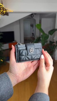 Tikattu musta nahkalompakko hopeisella vetoketjulla ja logokoristeella, jossa on kompakti suorakaiteen muoto ja sileä pinta.