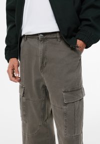 Cargo-broek in gedempt olijfgroen katoen. Kenmerkt grote zijzakken, een recht ontwerp en zichtbare stiknaden. Knopsluiting bij de taille.