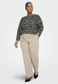 Dugi top s dugim rukavima u animal printu, ležernog kroja, u kombinaciji s bež širokim hlačama i crnim cipelama s špicastim vrhom, naglašavajući ležernu eleganciju.