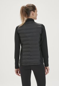 Sort isoleret vest med kviltet front, strækbare lange ærmer og høj krave. Glat tekstur med subtil glans, atletisk pasform.