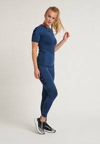 Haut de sport bleu marine et leggings avec des motifs texturés ; accents chevrons noirs sur les leggings ; associés à des chaussures de course noires et grises.