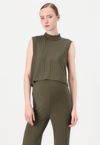 Top fără mâneci, de culoare verde măslin, cu dantelă ondulată și gât înalt. Materialul este moale și texturat, având un design stratificat și scurt.