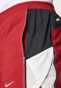 Κόκκινα και μαύρα αθλητικά σορτς με λευκή δίχτυνη λεπτομέρεια. Διαθέτουν ελαστική μέση και λευκή ραφή. Περιλαμβάνουν μικρό λογότυπο Nike ως διακοσμητικό στοιχείο.