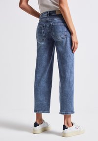 Jeans en denim de couleur bleu clair avec une coupe droite. Comprend deux poches arrière et une taille mi-haute. Portés avec des baskets blanches.