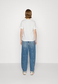 T-shirt branco de manga curta combinado com jeans de denim azuis oversized com um acabamento texturizado, usados com ténis prateados.