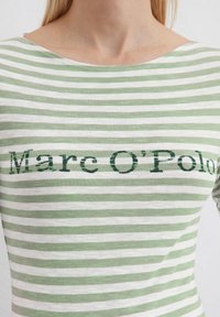 Camicia a righe verdi e bianche con scollo a barchetta e maniche corte. Presenta la scritta stampata "Marc O'Polo" in verde scuro.