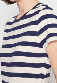Námořnická a krémová pruhovaná tričko s kulatým výstřihem, krátkými rukávy a jemnou, hladkou bavlněnou tkaninou. Horizontální pruhy jsou rovnoměrně rozmístěny.