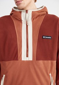 Felpa con cappuccio Columbia in tonalità ruggine e crema, con zip a un quarto sul fronte, morbido tessuto in pile e patch del logo sul petto.
