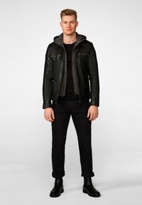 Schwarze Lederjacke mit grauem Kapuzenpullover, enges schwarzes T-Shirt, dunkle Jeans mit hochgeschlagenen Säumen und schwarze Stiefeletten. Einfacher, urbaner Stil.