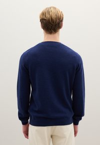 Maglione blu navy in morbida lana, con scollo rotondo, maniche lunghe e polsini a coste. Dettagli di cucitura sulle spalle.