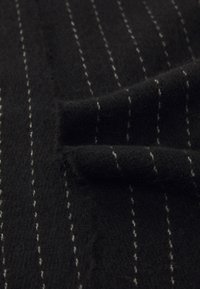 Uldstof i sort med hvide striber. Blød tekstur, let fuzzy, med tydelige lodrette linjer og en fold i materialet.