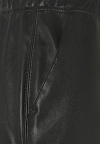 Zwarte leren broek met een gladde textuur, elastische tailleband, zijzakken en gedetailleerde stiksels langs de naden.