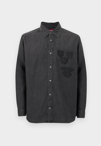 Μαύρο πουκάμισο από τζιν ύφασμα με κουμπιά στο μπροστινό μέρος, μακριά μανίκια, γιακά και τρία κεντημένα σημάδια στο αριστερό στήθος. Υφή υφάσματος.