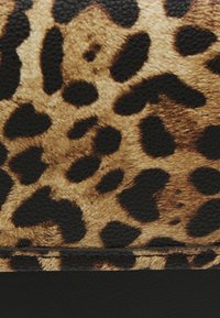 Kuhinoitettu kankaalla, jossa on leopardi-kuvio, mustia pilkkuja vaaleanruskealla taustalla, sujuvasti mustan materiaalin yläpuolella, ommeltu yhdessä vaakasuunnassa.