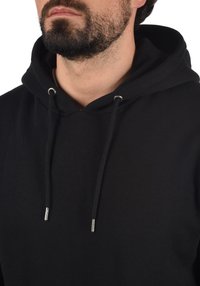 Sudadera negra con capucha que cuenta con un cierre de cordón con puntas plateadas, fabricada en un tejido suave, que presenta una textura lisa y un diseño clásico.