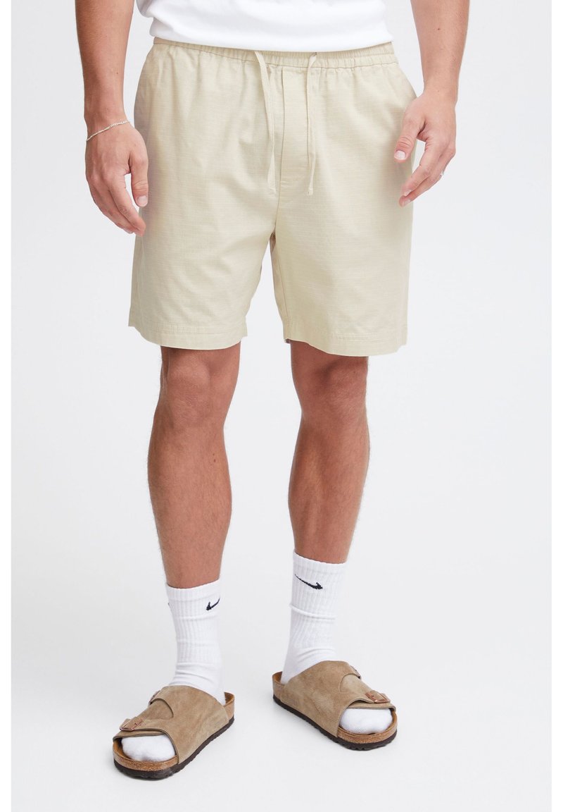 Light beige cotton shorts with an elastic waistband and adjustable drawstring. Worn with white socks and brown sandals.