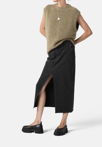 Top sin mangas beig, con cuello alto, falda de mezclilla negra con abertura lateral, zapatos negros de suela gruesa, collar minimalista de plata.