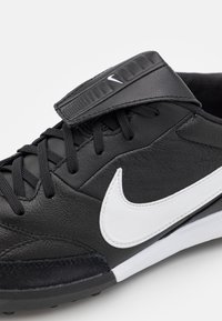 Black leather athletic shoe with white Nike swoosh, textured surface, laces, and adjustable strap. Features a sturdy heel and traction outsole.