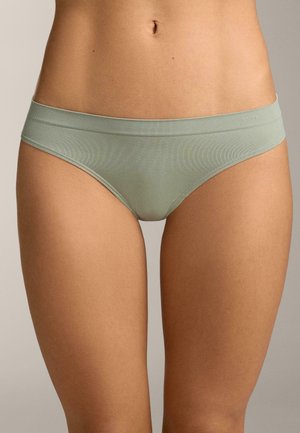 Žena u svijetlozelenom bešavnom hipster donjem rublju, prikazana od struka do sredine bedra na neutralnoj pozadini.