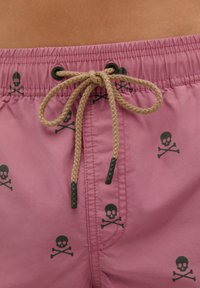 Pantaloni scurți de înot roz, cu talie ajustabilă, prezentând un model cu cranii și oase încrucișate negre. Realizați dintr-un material neted cu o textură ușoară.