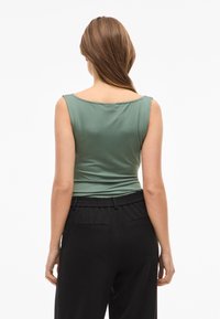 Top ajustado verde con escote amplio y sin mangas, combinado con pantalones negros de cintura elástica que cuentan con bolsillos traseros.