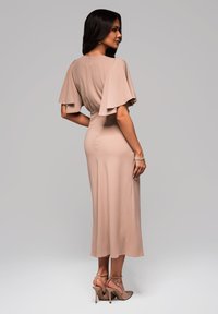 Nude midi sukienka z falbaniastymi rękawami, dopasowaną górą, miękkim materiałem i zamkiem błyskawicznym z tyłu. Zestawiona z sandałami na wysokim obcasie z paskami.