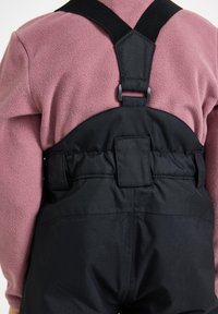 Sorte vandtætte arbejdsbukser med justerbare stropper, parret med en lyserød fleece-top. Bemærkelsesværdig syning og glat stofstruktur synlig.