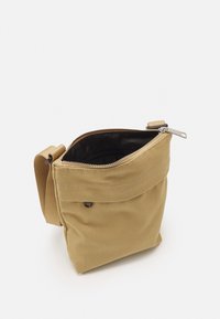 Khaki kanvas taske med en top lynlås, justerbar rem og en glat sort indvendig. Har en lille lomme indeni til organisering.