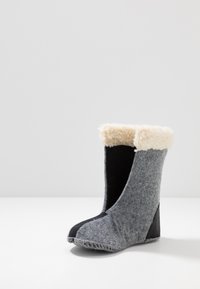 Szara filcowa botka z czarną dolną częścią i miękkim kremowym futerkiem na górze. Posiada zaokrąglony czubek i widoczne detale przeszycia.