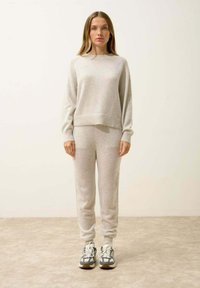 Jasnoszary sweter z dzianiny i pasujące dresy, z prążkowanymi mankietami i dołem. Model nosi szare sneakersy z czarnymi akcentami. Gładka tekstura.