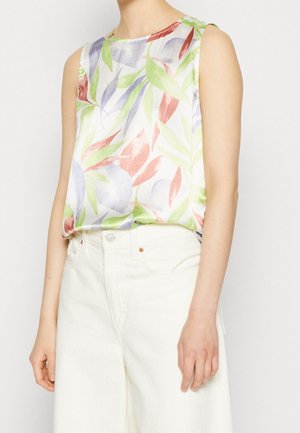 Blouse blanche sans manches à motif de feuilles vertes, violettes et rouges, rentrée dans un pantalon blanc taille haute à jambes larges.