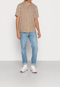 Bruine en witte gestreepte shirt met korte mouwen, met een knoopsluiting aan de voorkant, gecombineerd met lichtblauwe jeans en witte sneakers met bruine accenten.