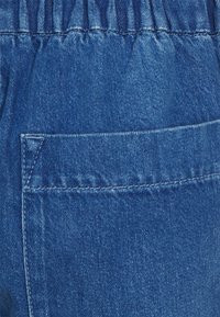 Tela de mezclilla azul con una banda elástica en la cintura y un gran bolsillo rectangular con costuras reforzadas.