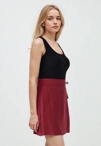 Zwarte geribbelde tanktop gecombineerd met een bordeauxrode flared rok. De rok heeft een strik taille, een gladde textuur en een casual pasvorm.