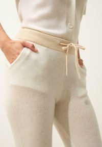 Neulehousut vaaleassa valkoisessa, jossa on beige nyöri vyötäröllä, sivutaskut ja pehmeä, teksturoitu kangas.