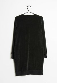 Vestido de terciopelo negro con mangas largas, cuello redondo y puños rematados. La tela texturizada ofrece una superficie suave. Cuelga de un gancho negro.