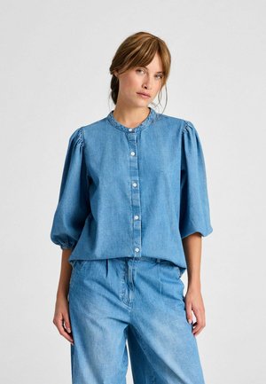 Svetlo modra denimska srajca s napihnjenimi kratkimi rokavi, zaobljenim ovratnikom in gumbnim zapiranjem spredaj. Mehka tekstura in sproščen kroj. Usklajena z denimski hlačami.