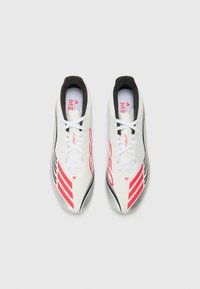 Witte voetbalschoenen met zwarte en roze accentstrepen, voorzien van een gestroomlijnd ontwerp, veters en een gladde, textuur afgewerkte uitstraling.